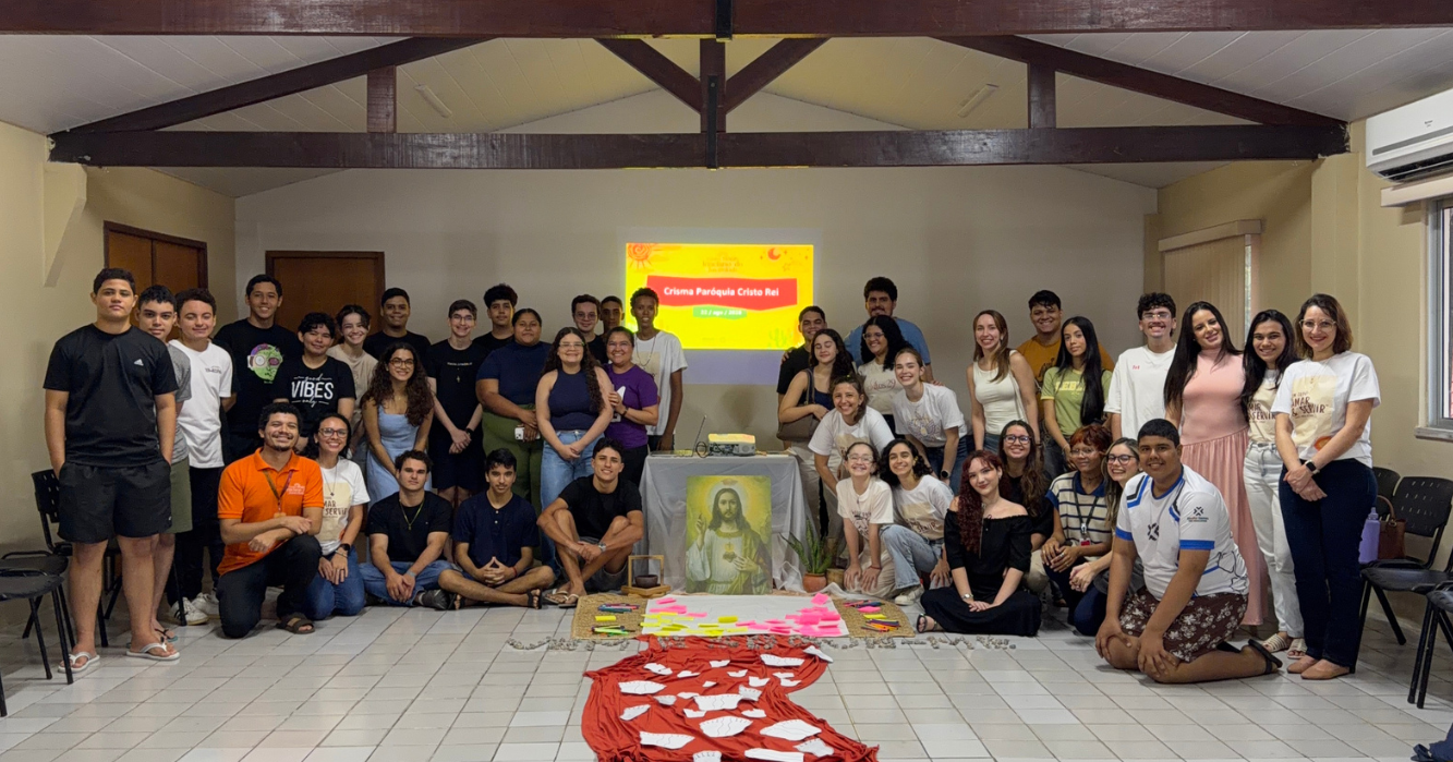 Grupo de jovens e adultos reunido durante encontro de preparação para a Crisma da Paróquia Cristo Rei, em torno de um espaço de oração com imagem de Jesus e materiais utilizados na atividade.